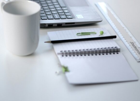 black pencil on ruled notepad beside white ceramic mug and gray laptop computer